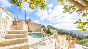 Ein Poolbereich mit Stufen, die zu einer Terrasse führen, ein Holzstuhl und Blick auf eine Berglandschaft.