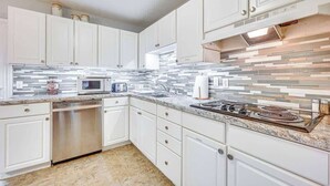 Una cocina moderna con armarios blancos, lavavajillas de acero inoxidable, microondas, cocina a gas y salpicadero de azulejos.