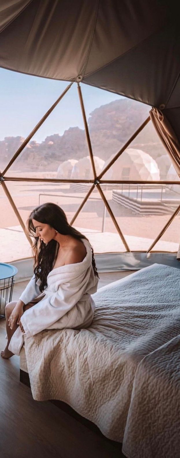 A person sitting on a bed inside a tent with a view of mountains.