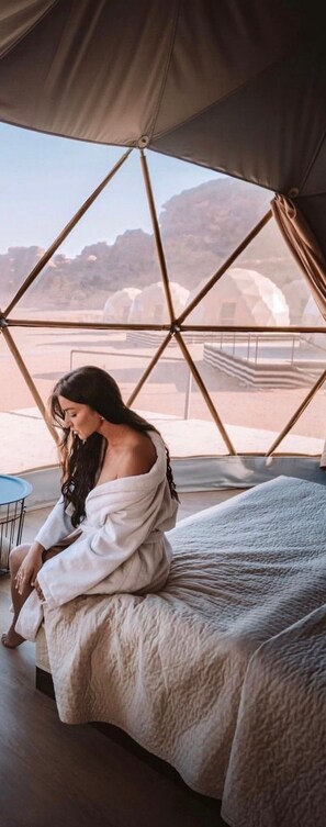 A person sitting on a bed inside a tent with a view of mountains. - Tradition Of Wadi Rum Camp (Wadi Rum)