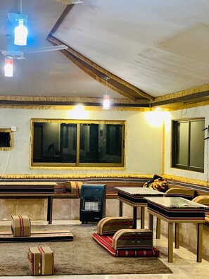 A room with a large window, a ceiling fan, and a bookshelf. - Tradition Of Wadi Rum Camp (Wadi Rum)