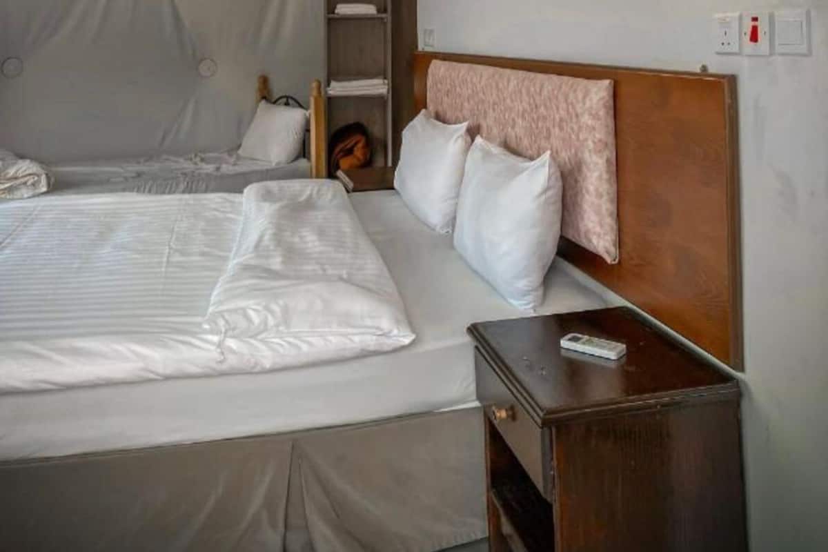 A hotel room with a large bed, a wooden headboard, a nightstand, and a shelf with a book.