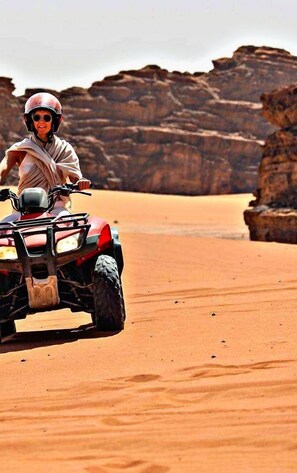 A person riding an ATV in a desert landscape with rocky formations. - Tradition Of Wadi Rum Camp (Wadi Rum)