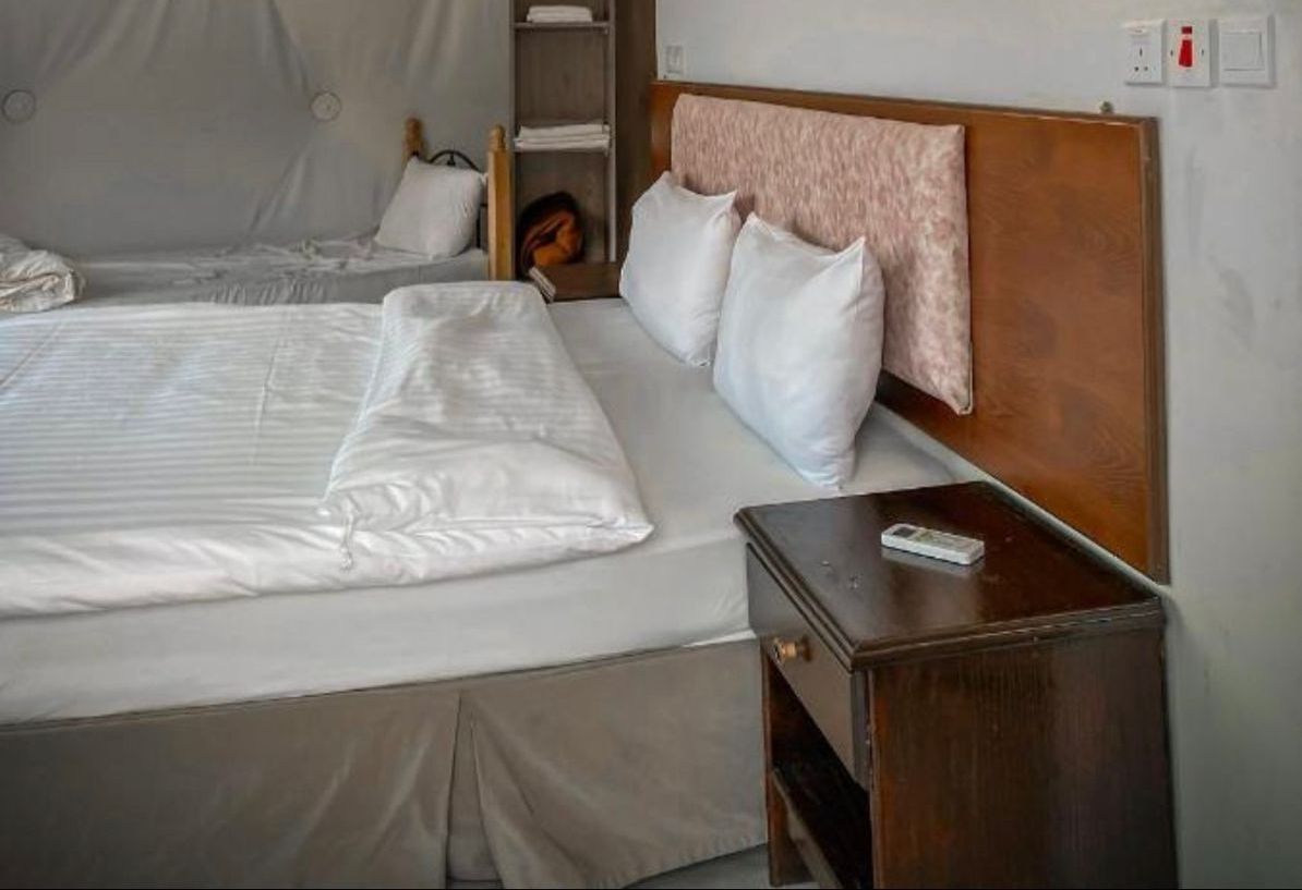 A hotel room with a large bed, a wooden headboard, a bedside table, and a wall-mounted power outlet.