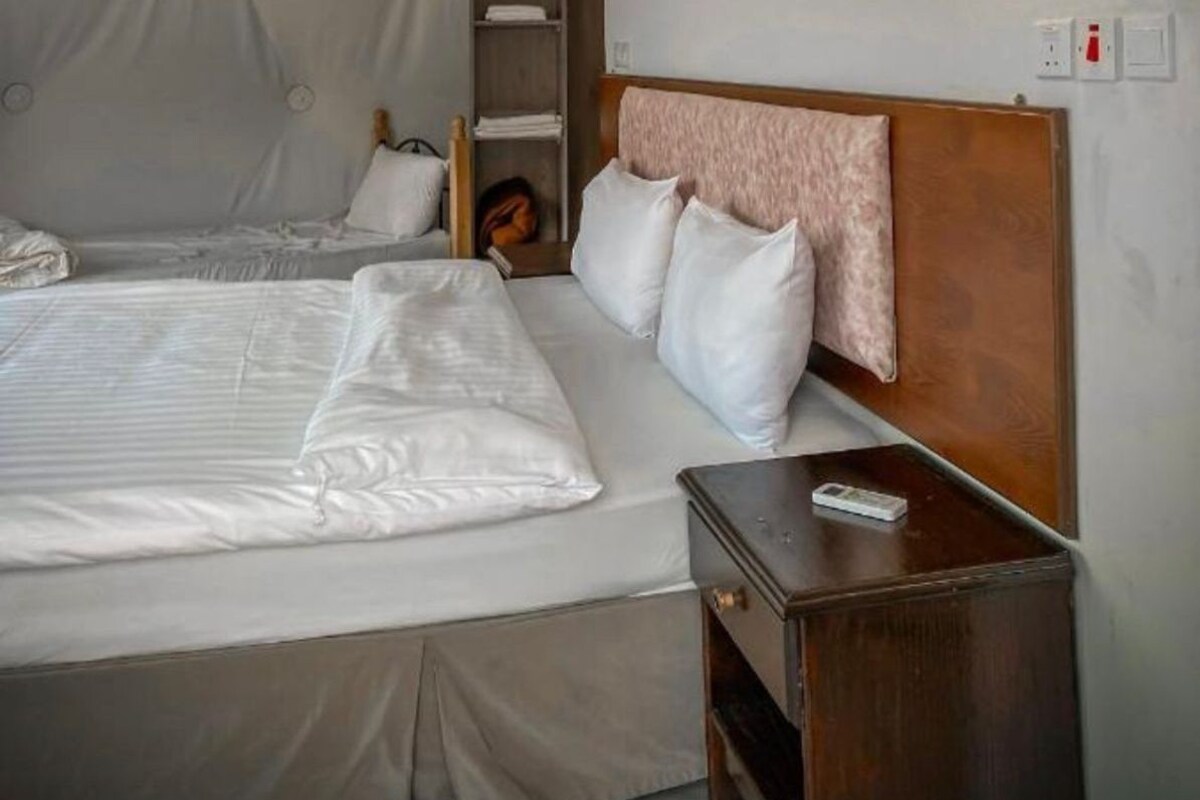 A hotel room with a large bed, a wooden headboard, a nightstand, and a shelf with a book.