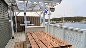 Une terrasse en bois avec une table de pique-nique et un espace barbecue, donnant sur une étendue d’eau.