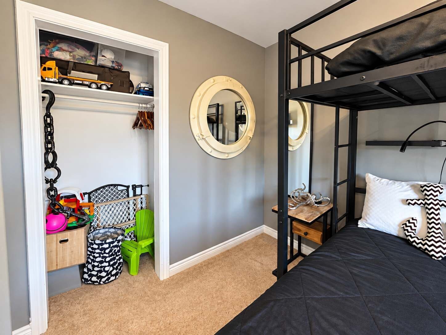 A bunk bed with a black mattress, a wooden nightstand, a mirror, and a toy car shelf.