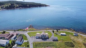 Vue aérienne d’une propriété située sur la côte, avec une grande maison, un garage et un petit bateau amarré près du rivage.