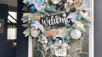 Una porta blu scuro con una ghirlanda decorativa che include un cartello con la scritta 'Welcome', conchiglie e rami di pino.
