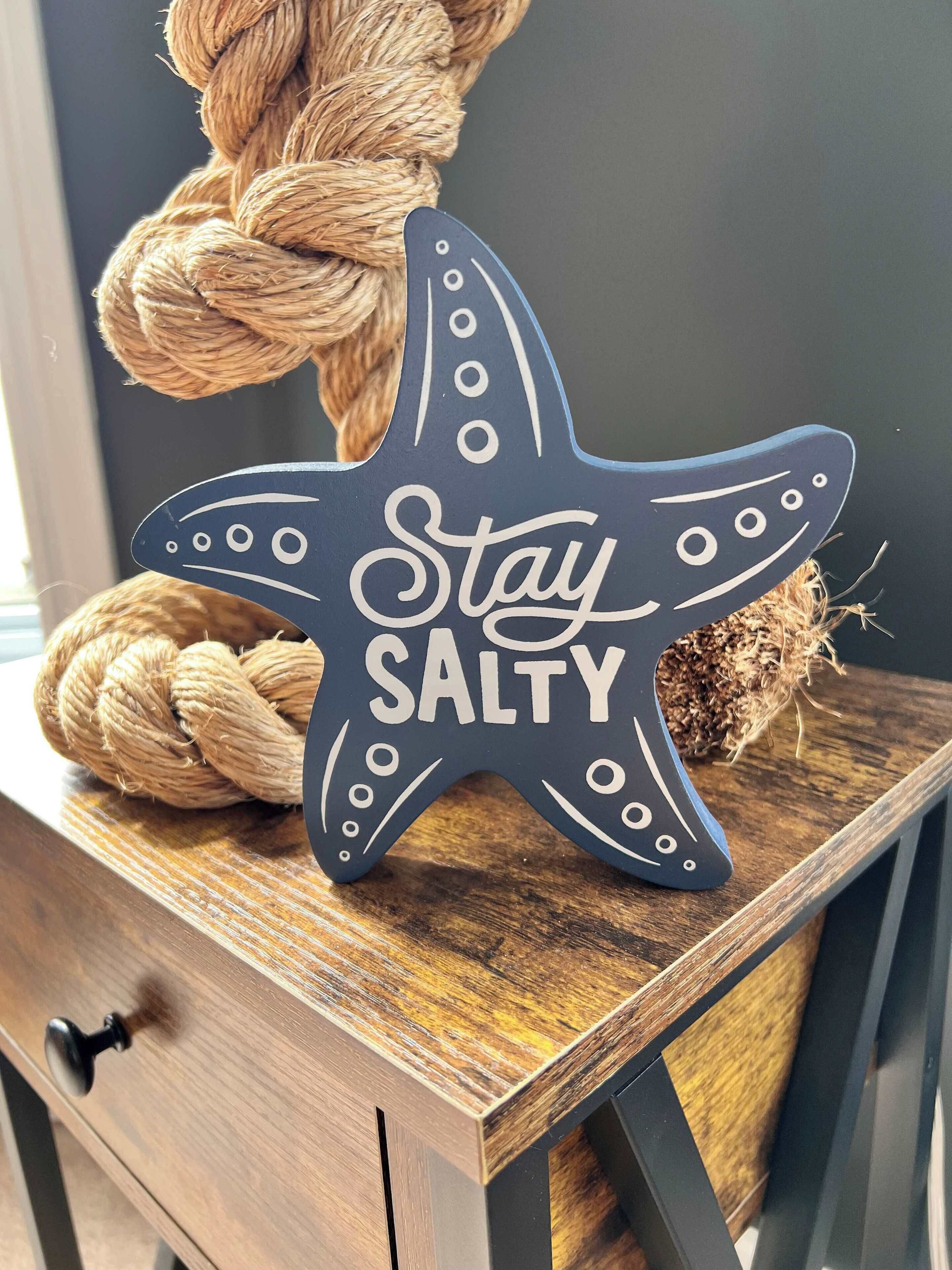 A starfish-shaped sign with the text "Stay SALTY" on a wooden surface.