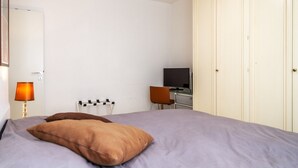 Ein Schlafzimmer mit Bett, Schreibtisch, Stuhl, Fernseher und Kleiderschrank.