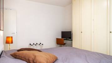 Ein Schlafzimmer mit Bett, Schreibtisch, Stuhl, Fernseher und Kleiderschrank.