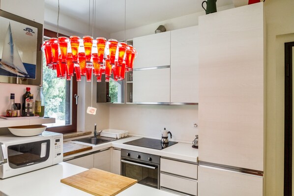 A modern kitchen with white cabinetry, a microwave, a stove, and a unique red pendant light.