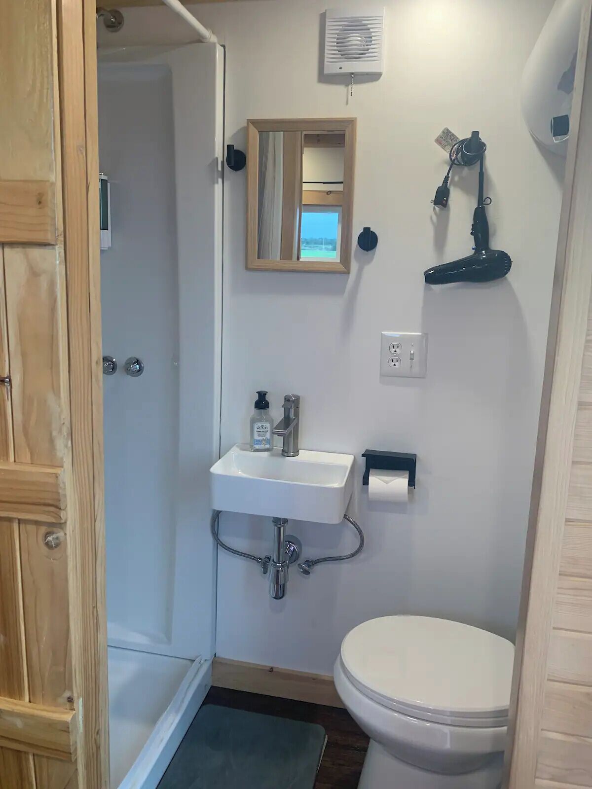 A small bathroom with a white sink, mirror, and toilet. There is a shower door and a towel rack visible.