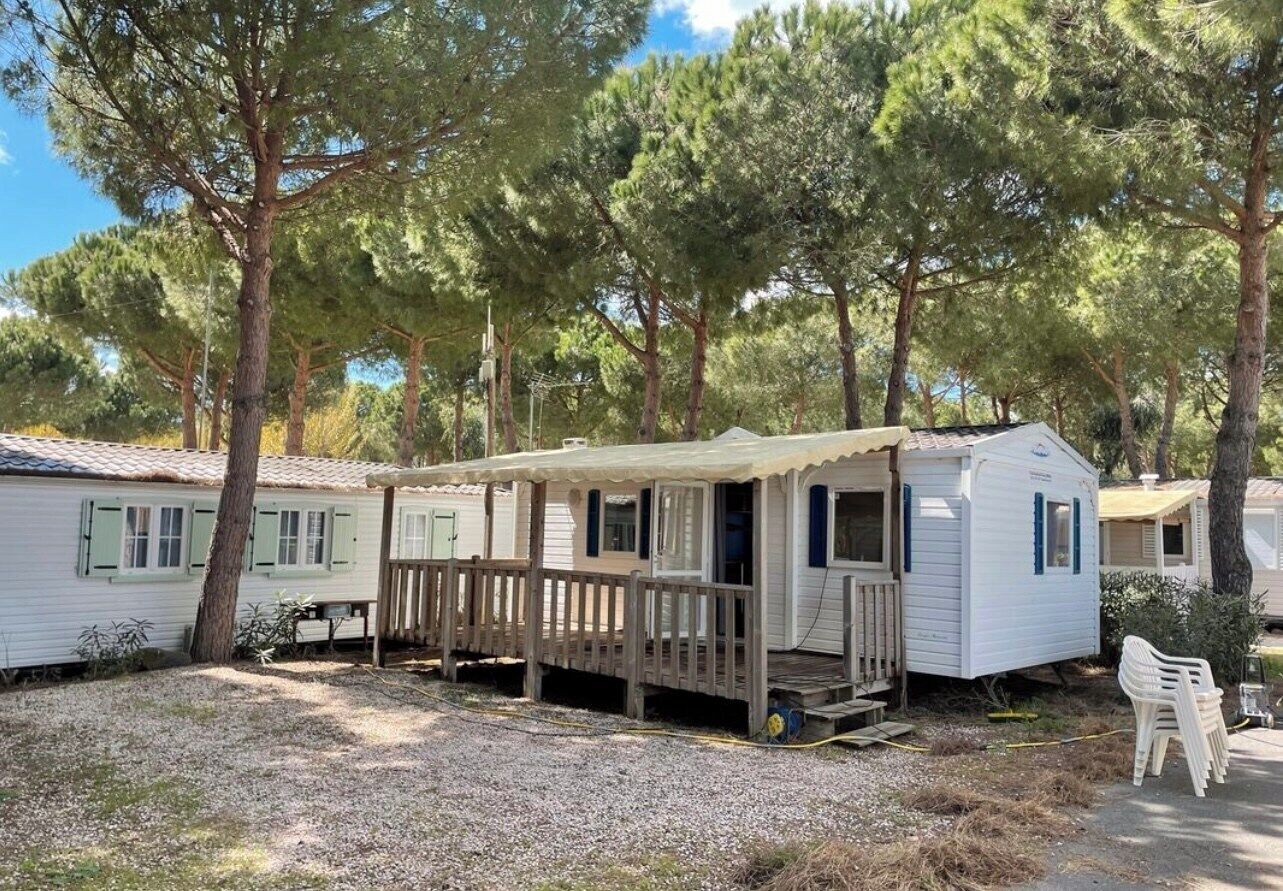 Ein Mobilheim mit Veranda und kleiner Terrasse, umgeben von Bäumen.