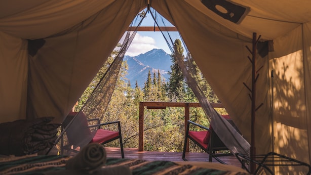 Ein Zelt mit Blick auf Berge und Bäume. Im Inneren ein Holztisch und zwei Stühle.