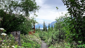 Ein Kiesweg schlängelt sich durch üppiges Gr ün und Wildblumen zu einer Holzhütte.