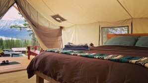 Eine Zeltunterkunft mit Bett, kleinem Tisch und Bergblick.