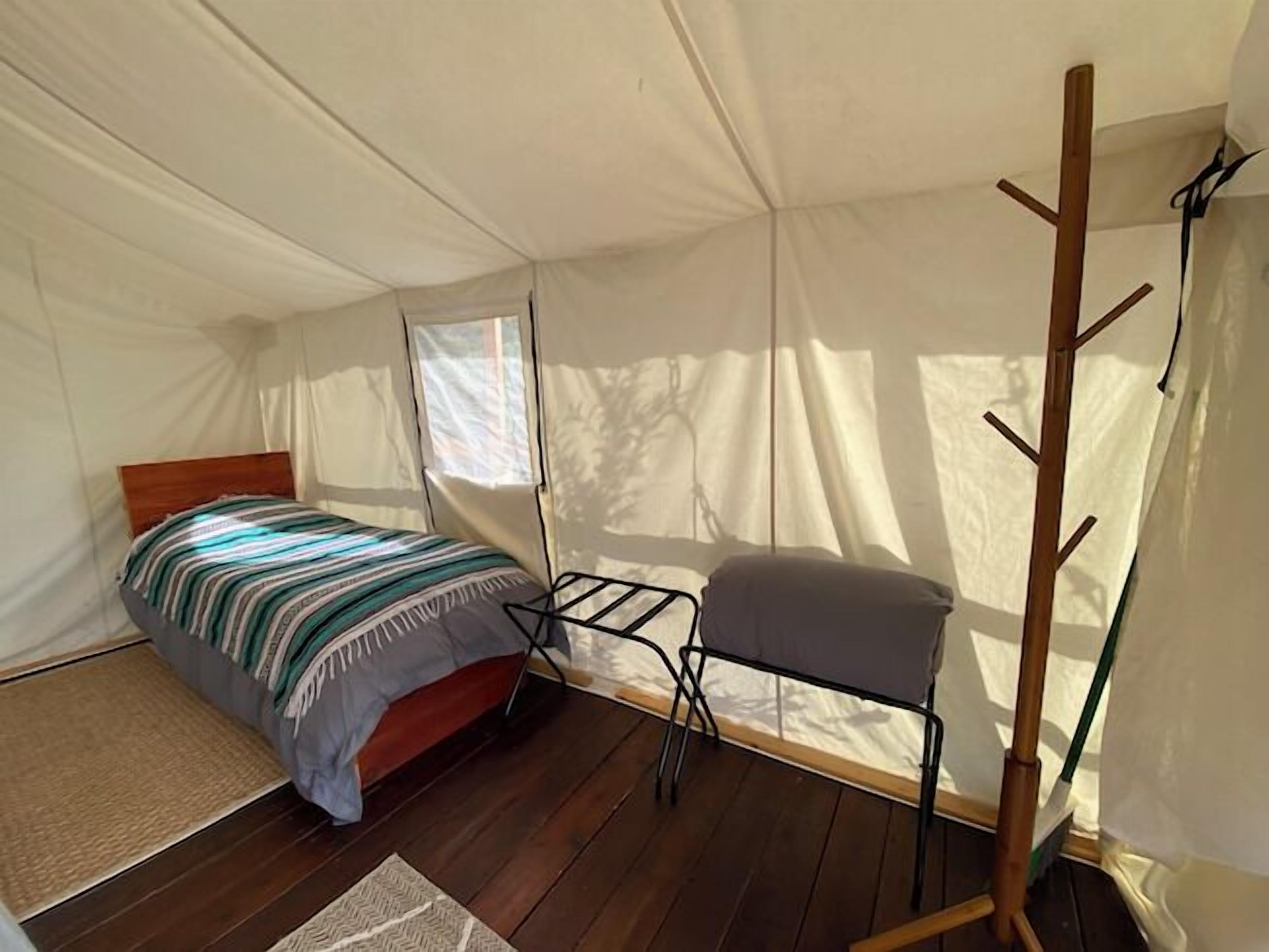 A tented room with a bed, a chair, and a drying rack.