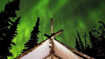 A tent with two red chairs and a wooden deck, set against a backdrop of the Northern Lights.