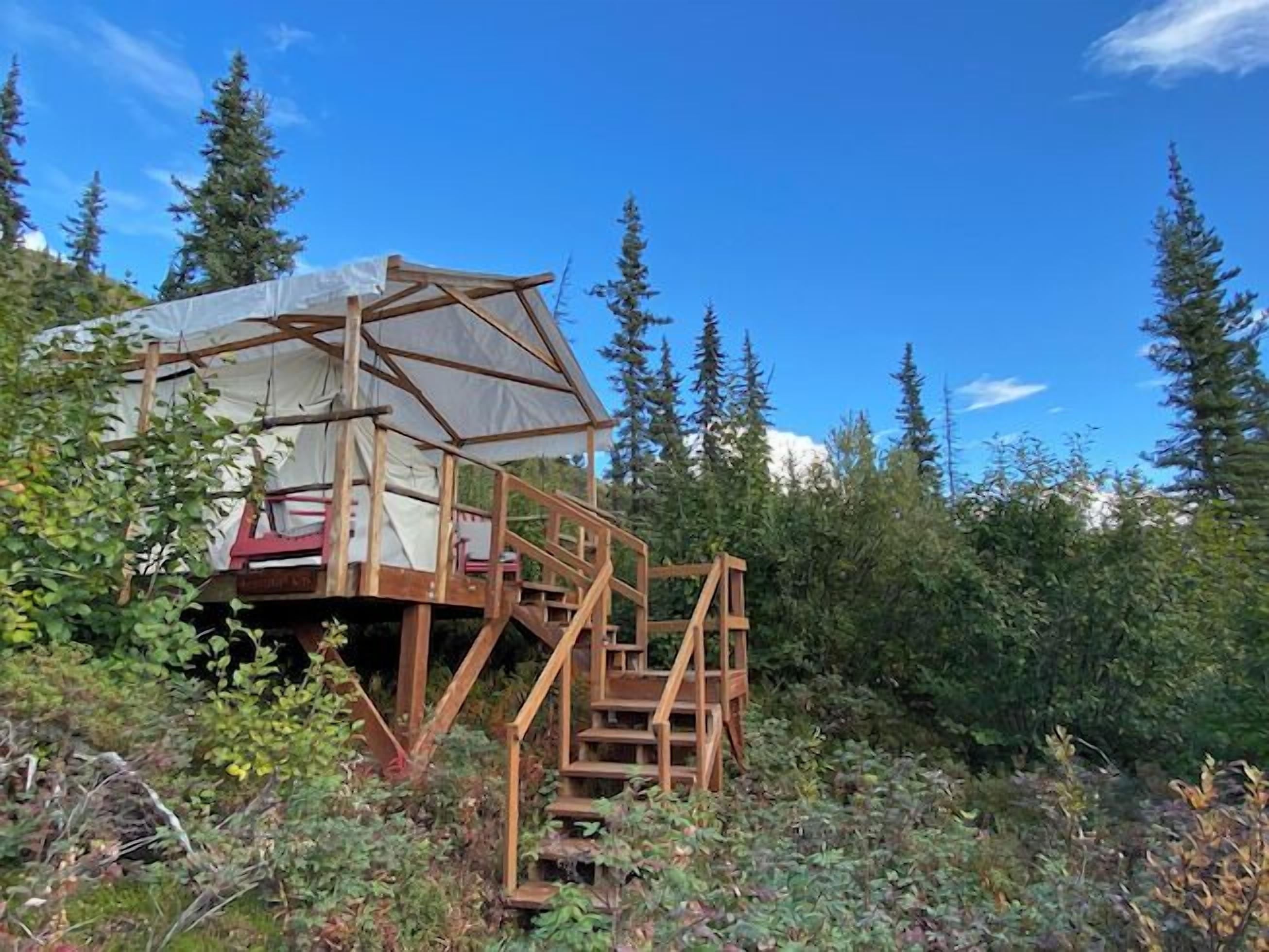 A wooden cabin with a covered porch and a staircase leading to a deck.