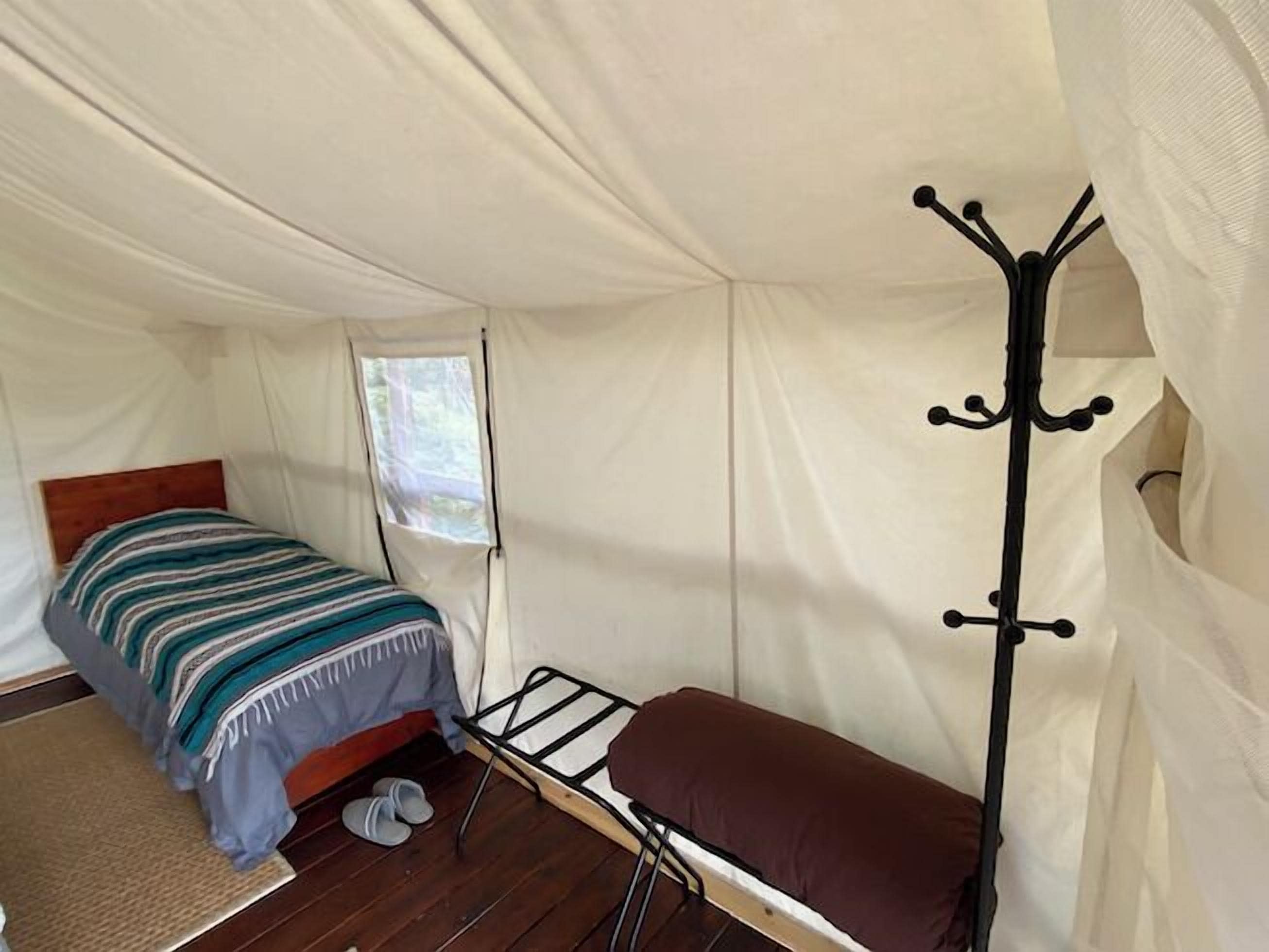 A tent with a single bed, a small window, and a metal coat rack.
