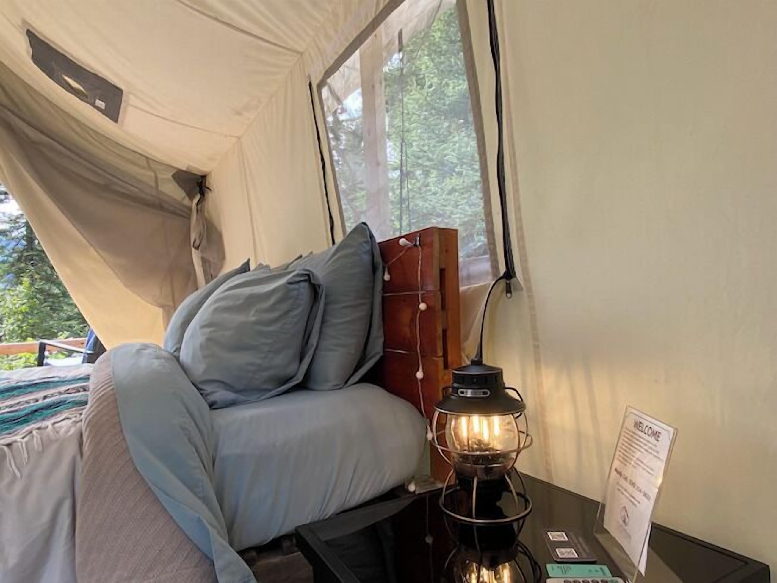 Een tent met een bed, kussens, een lantaarn en een bord met een welkomstboodschap.