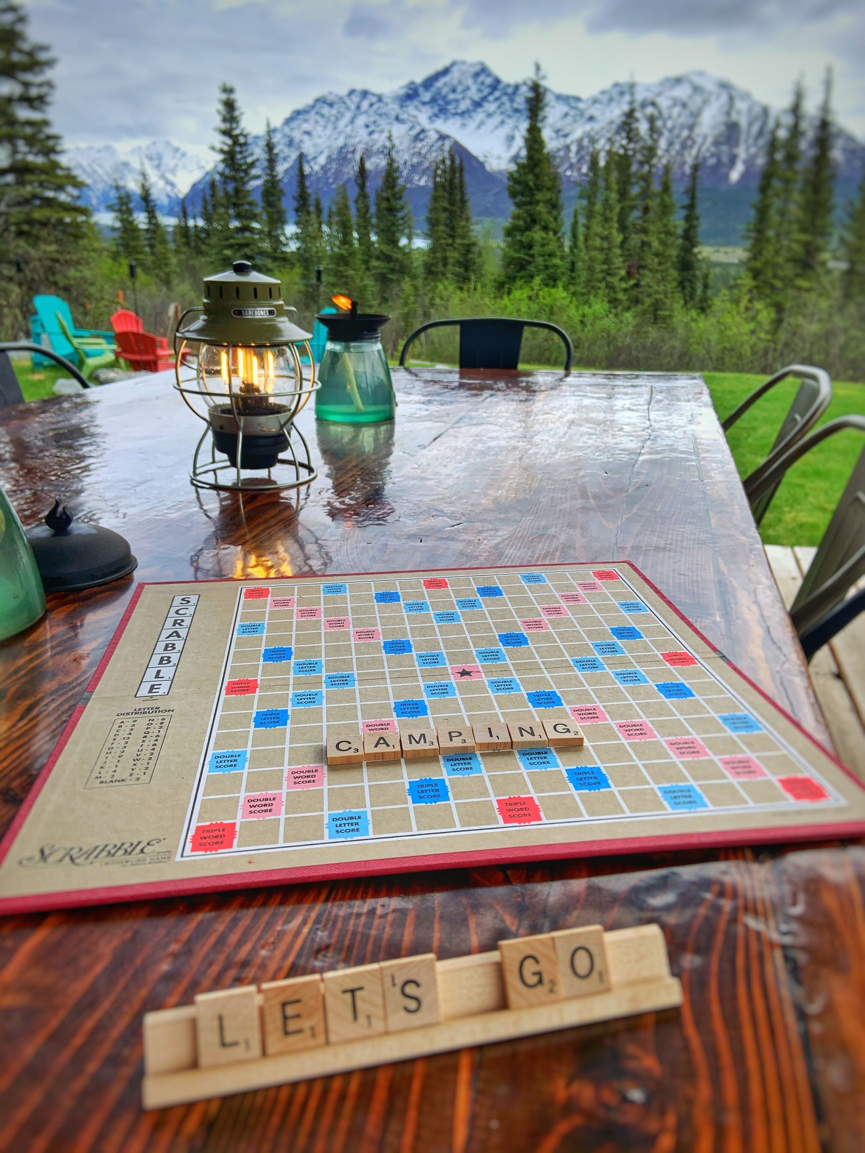 A Scrabble game on a wooden table with a scenic mountain view in the background.