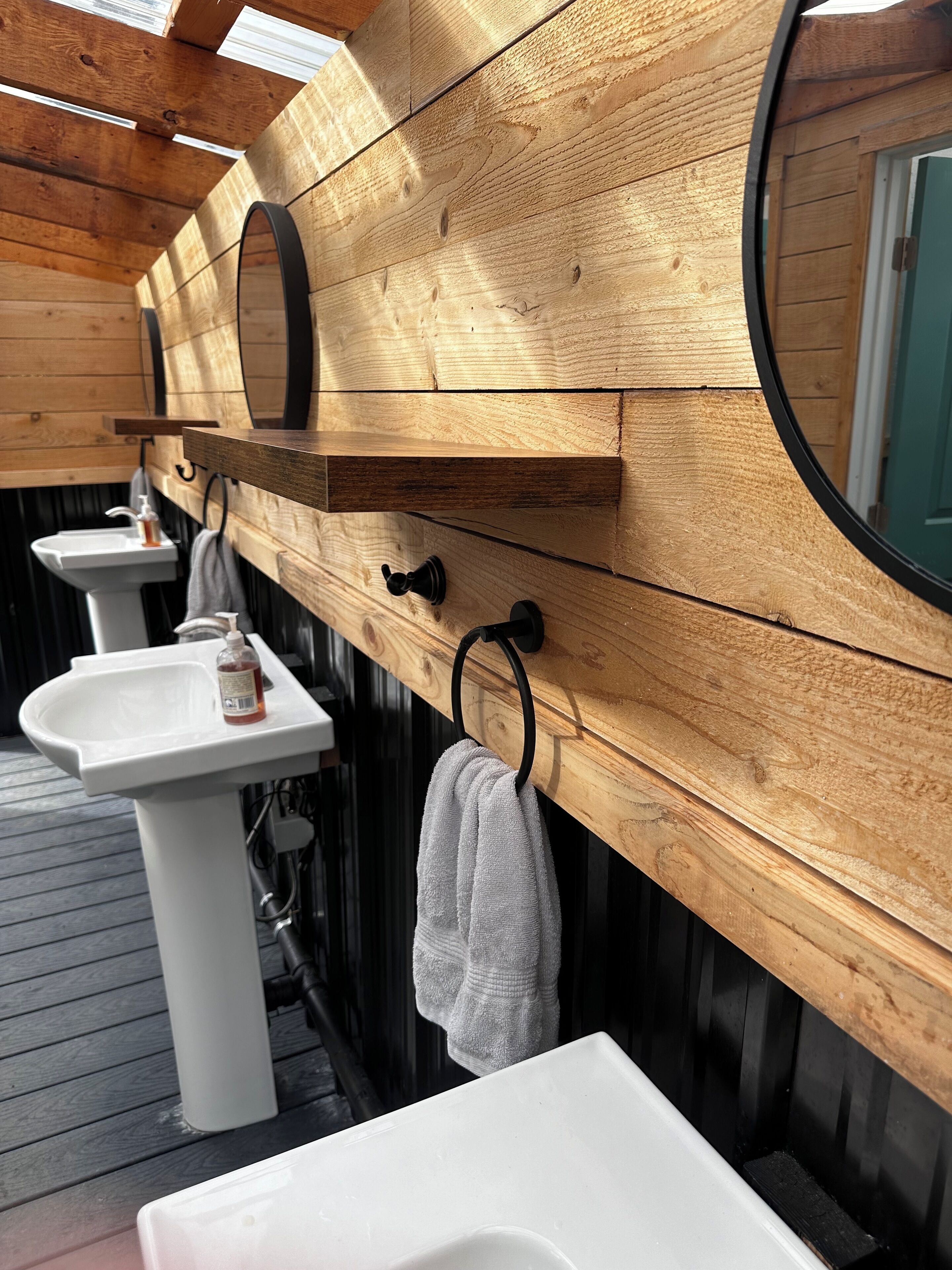 A wooden bathroom with two sinks, a mirror, and towels hanging on hooks.