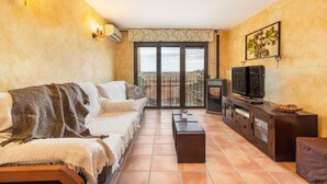 Ein Wohnzimmer mit einer Couch, einem Couchtisch, einem Fernseher auf einer Holzkommode und einem Balkon mit Blick.