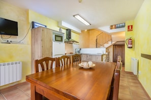 Un comedor con mesa y sillas de madera, una cocina con microondas y estufa, y un televisor montado en la pared.