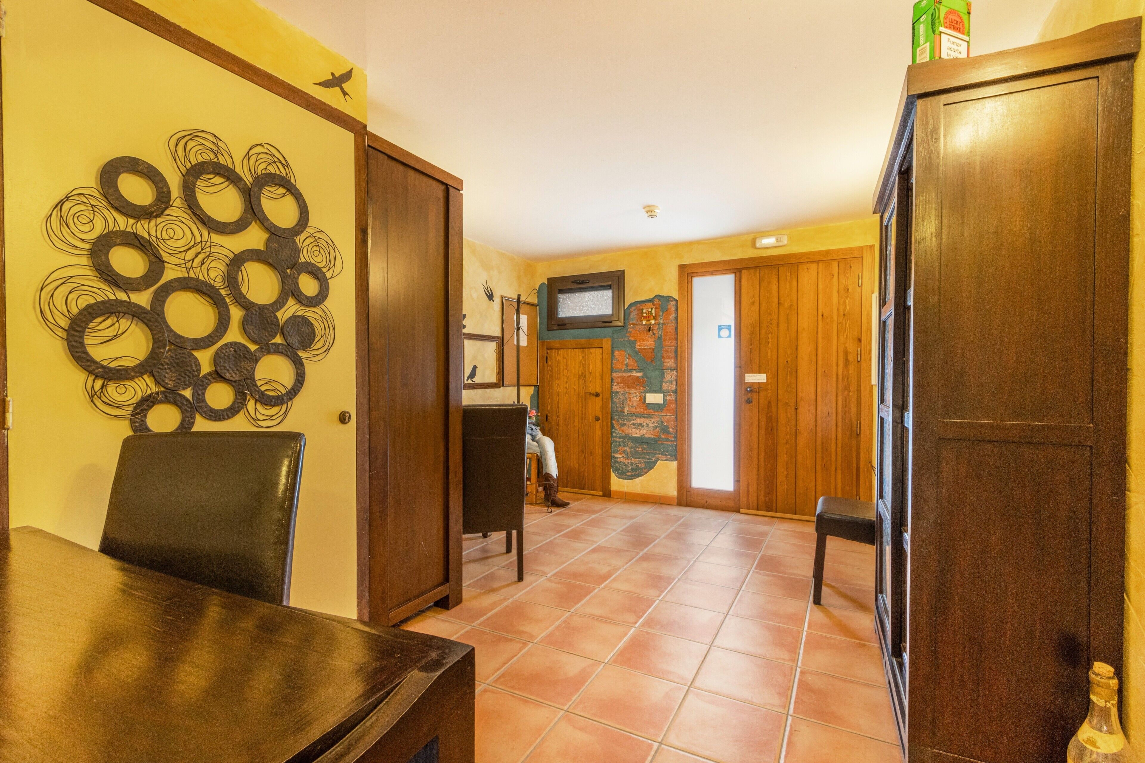 Un área de comedor con una mesa y sillas de madera, una obra de arte abstracta colgada en la pared y un televisor también en la pared.
