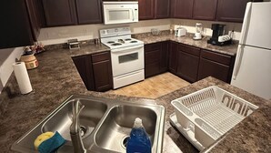 Una cocina con armarios de madera oscura, una estufa blanca, un microondas, un lavabo con escurreplatos y una encimera con varios electrodomésticos.