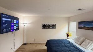 Un dormitorio con cama, televisor montado en la pared, lámpara de pie y un cuadro.