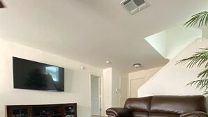 Una sala de estar con un sofá de cuero marrón, un televisor de pantalla plana montado en la pared y una mesa de centro de madera.