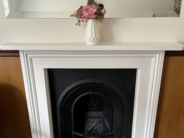 Une cheminée blanche surmontée d’un vase blanc contenant des fleurs roses.