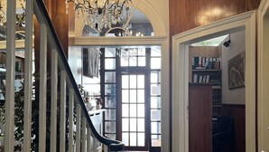 A grand staircase leading to a room with a chandelier, a bookshelf, and a door leading outside. - The Marker Hotel (London)