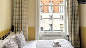 A hotel room with a bed, a window with curtains, a radiator, and a flat-screen TV mounted on the wall. - The Marker Hotel (London)