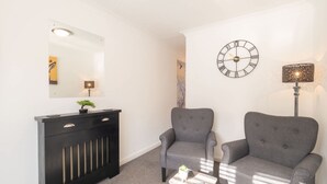 A modern living room with a black console table, two grey armchairs, a small white table, a wall clock, and a mirror. - Host Stay St Martin s Road (Canterbury)