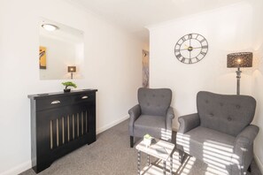 A modern living room with a black console table, two grey armchairs, a small white table, a wall clock, and a mirror. - Host Stay St Martin s Road (Canterbury)