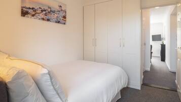 A bedroom with a bed, white wardrobe, and a painting of a coastal town.