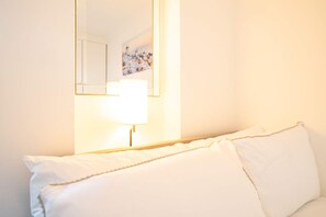 A white bed with a headboard, a bedside lamp, and a wall-mounted mirror reflecting a painting. - Host Stay St Martin s Road (Canterbury)