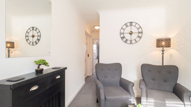A hallway with two grey armchairs, a black console table with a potted plant, and two wall clocks. - Host Stay St Martin s Road (Canterbury)