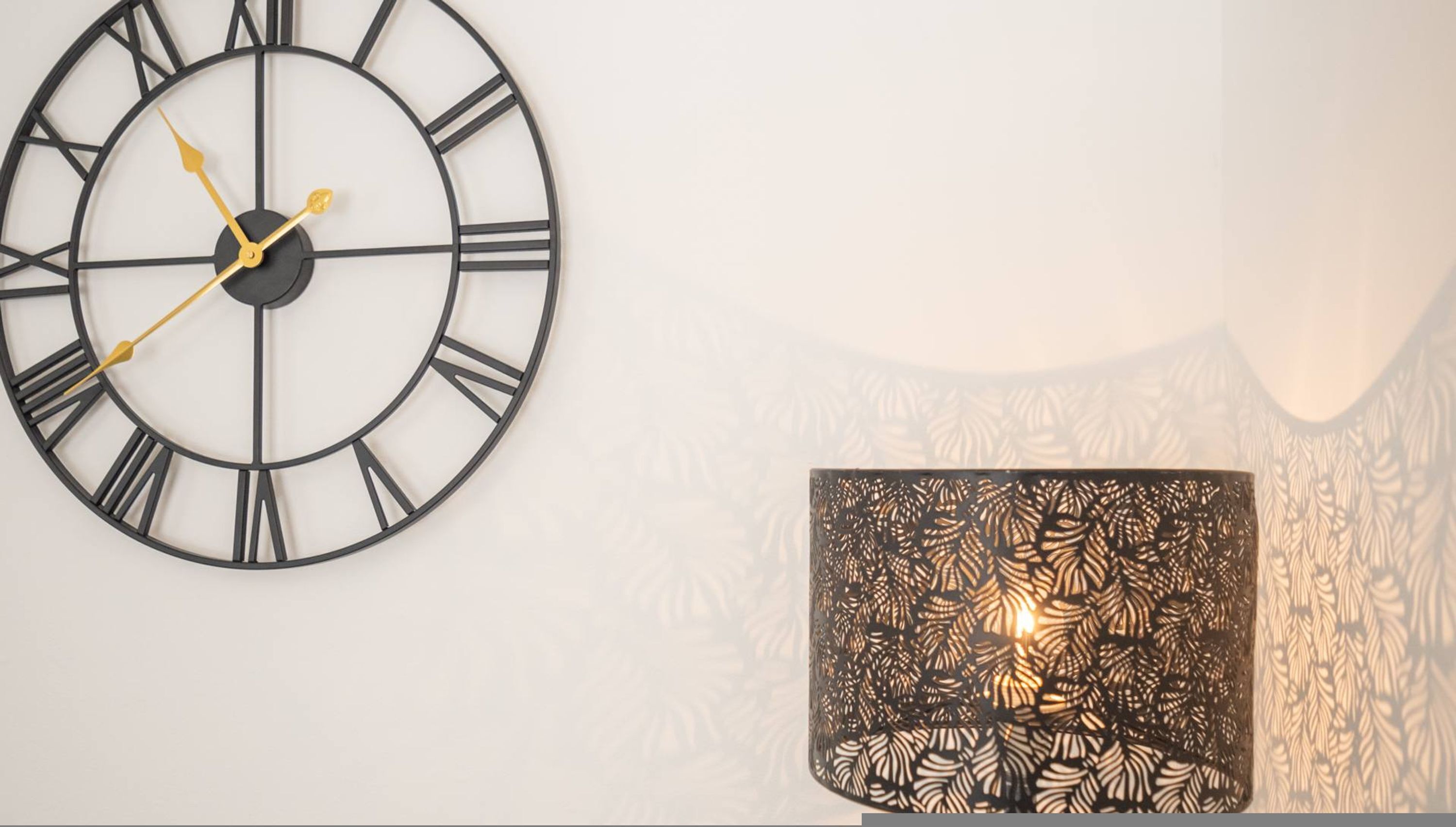 A wall clock with Roman numerals and a decorative wall lamp with a leaf pattern.