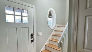 Una escalera con peldaños de madera y paredes blancas que conduce a una puerta con un ventanal.