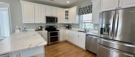 A modern kitchen with white cabinets, stainless steel appliances, and a marble countertop.