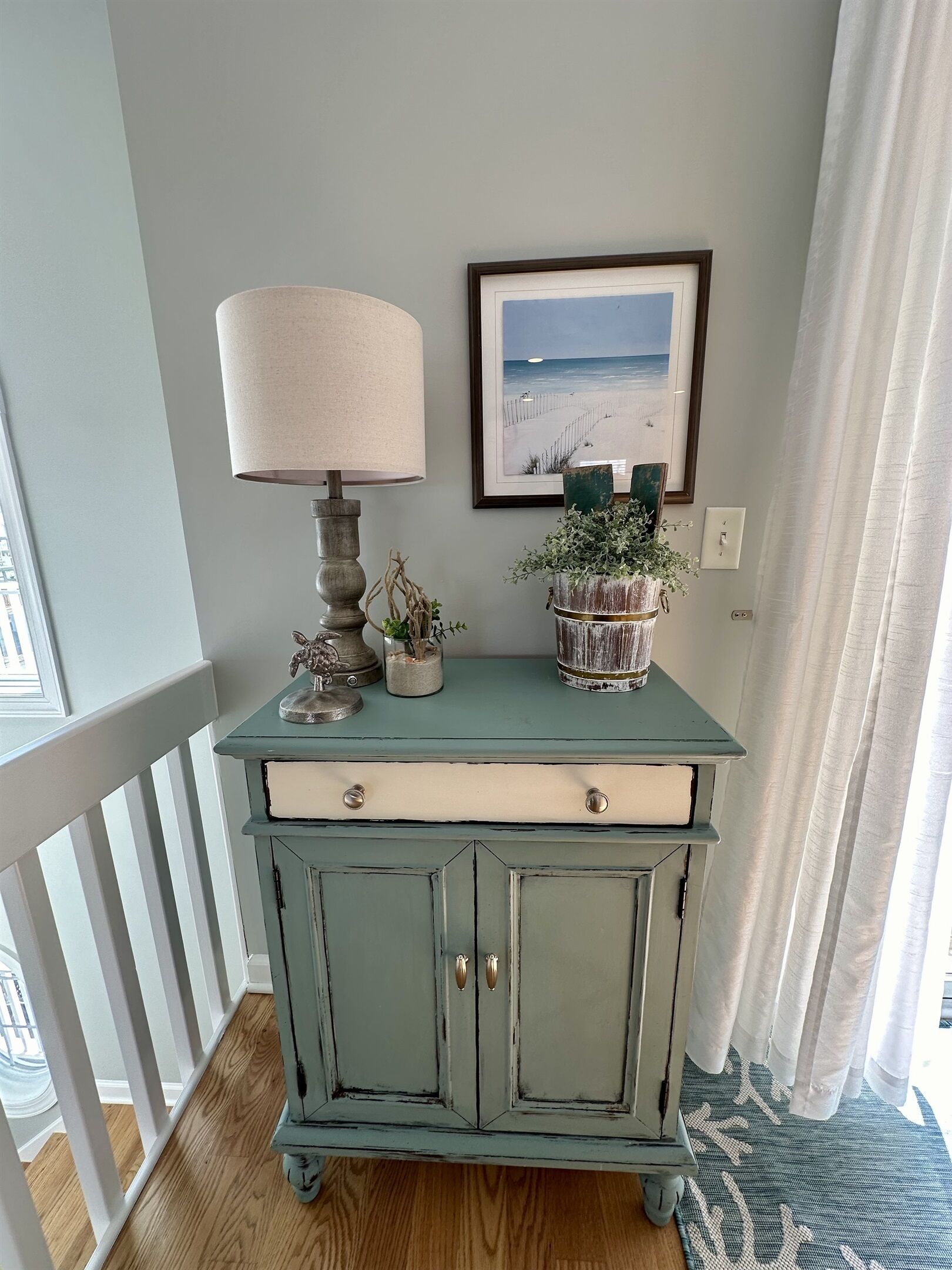 Une commode bleu sarcelle avec des tiroirs, une lampe et un tableau encadré accroché au mur.