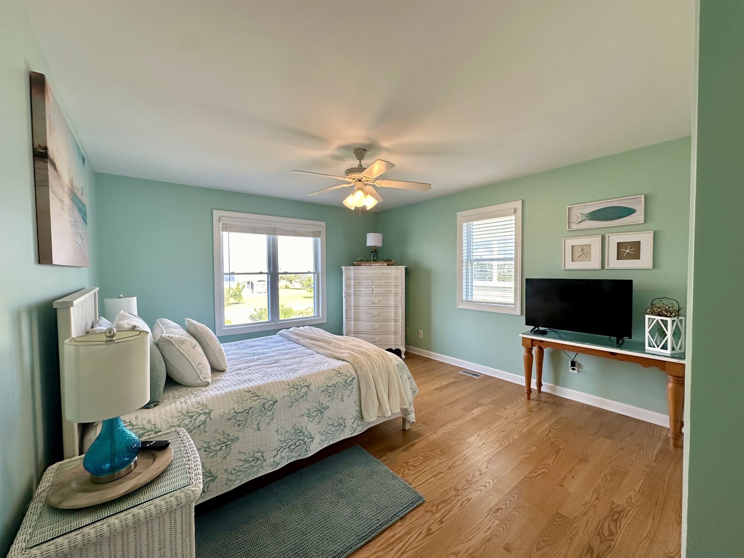 A bedroom with a bed, dresser, TV, and artwork on the wall.