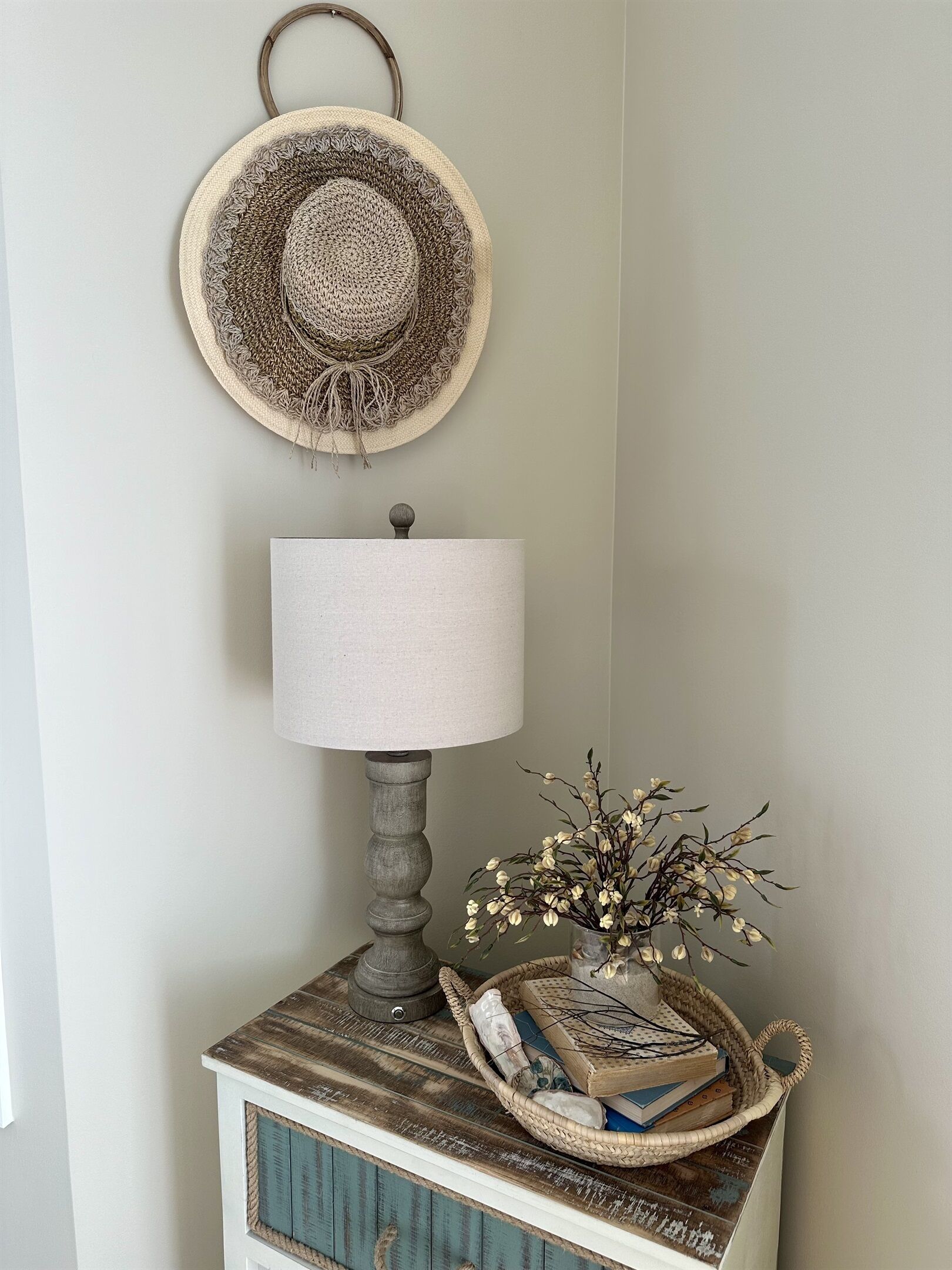 A corner with a lamp, a woven basket with books, and a wall-mounted hat.