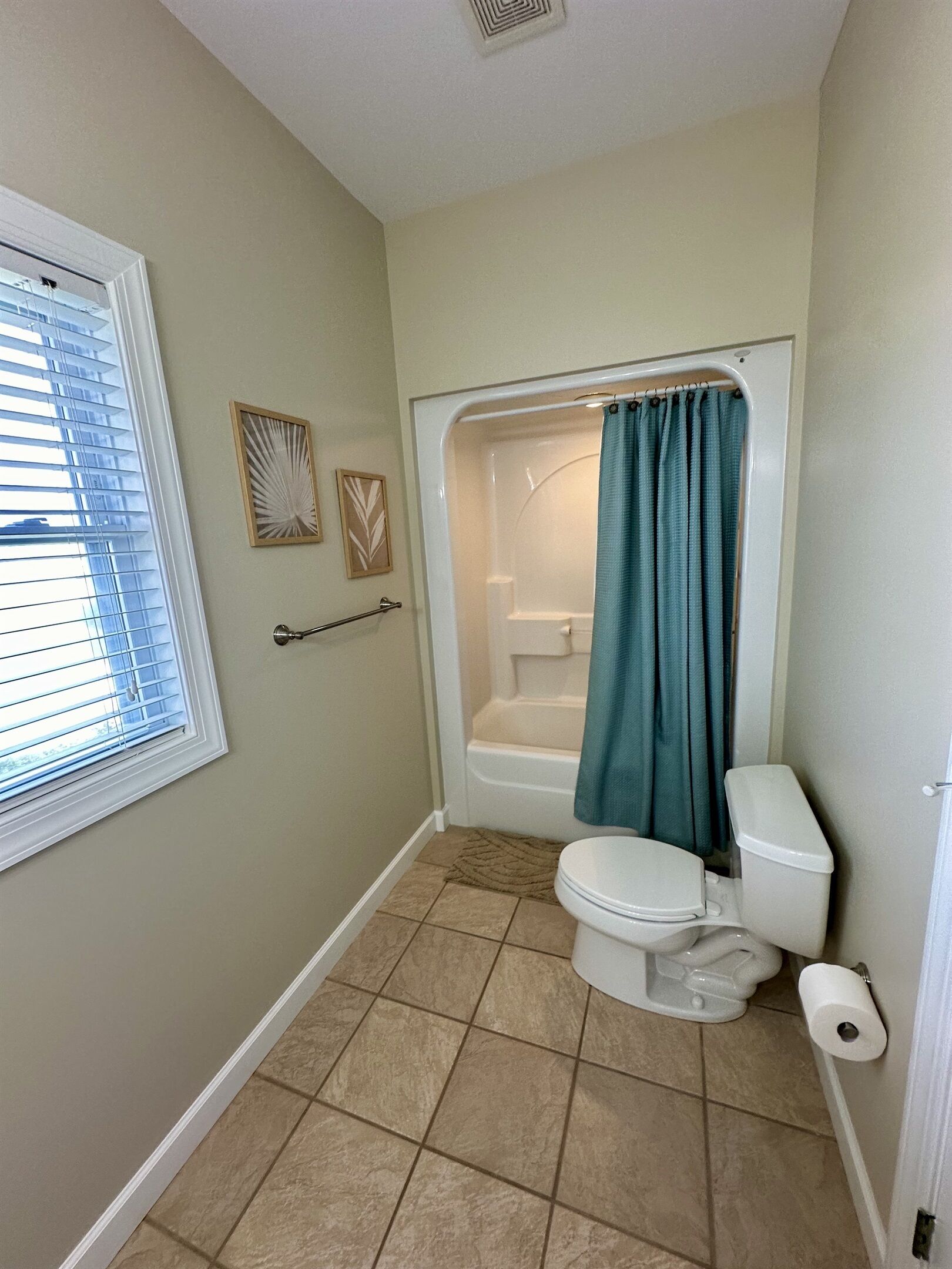 A bathroom with a bathtub, toilet, and a window with blinds.